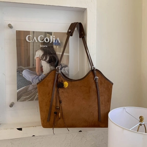 Close-up of brown suede tote bag with yellow pompom and tassel on a beige background