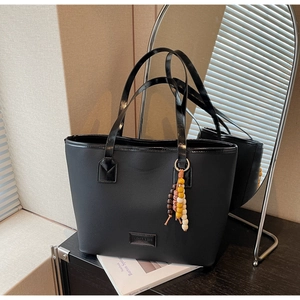 Détail du sac cabas noir texturé avec breloque en perles et écusson du logo de marque