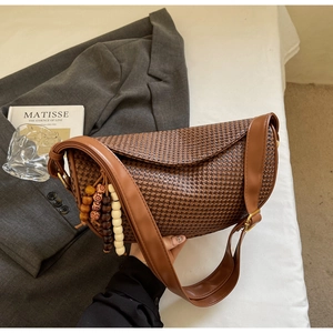 Detail of a brown houndstooth crescent bag with wide leather strap and beaded charm