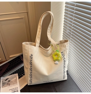 Detail view of canvas tote bag with black lettering and a yellow floral charm pendant