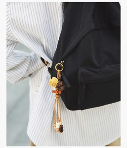 Detail of black nylon backpack featuring a colorful tassel charm with plush pom-poms