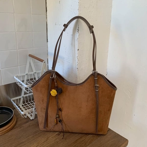 Detail of a brown suede tote bag featuring a leather strap and floral tassel charm