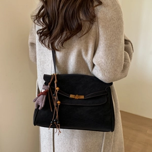 Detail of black suede handbag with gold lock, plush bear charm and beaded tassels