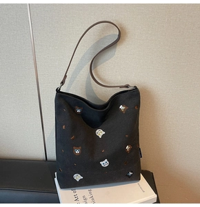 Close-up of black canvas tote bag featuring colorful animal embroidery and brown leather strap