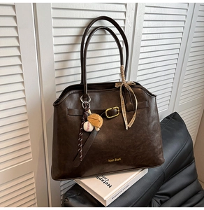 Detail of dark brown faux suede tote bag with gold buckle, ribbon, and baseball charm