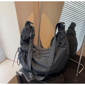 Detail of plaid canvas hobo bag showing adjustable strap and textured side drawstring