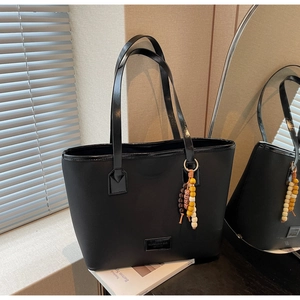 Détail du sac cabas en tissu noir avec poignées en cuir et breloque en perles de bois