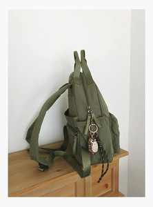 Detail view of army green nylon backpack with side pockets and owl charm on a wooden surface