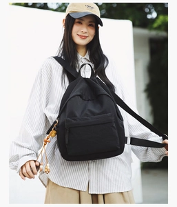 Minimalist black backpack with wooden bead tassel charm shown on a model outdoors
