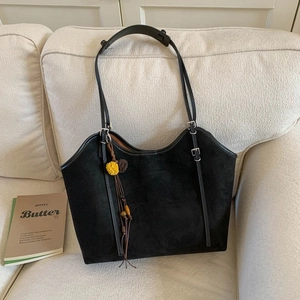 Close-up of black suede tote bag with silver buckles and a floral tassel charm on sofa