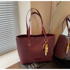Détail du sac cabas bordeaux avec texture cuir et pompon en perles de bois