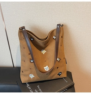 Detail of a brown canvas tote bag featuring colorful cat embroidery and leather handle