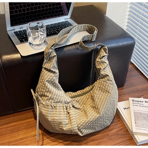Detail view of brown checkered canvas hobo bag on floor with a laptop and books