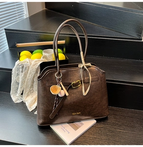 Detail of dark brown faux suede tote bag with gold logo and baseball charm on wood stairs