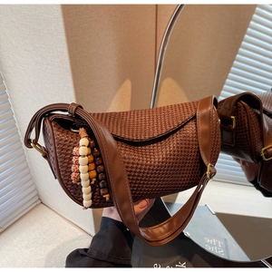 Detailed close-up of dark brown woven dumpling bag with decorative beaded tassel charm