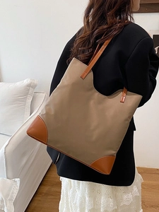 Khaki large capacity nylon tote bag with brown leather trim shown on shoulder