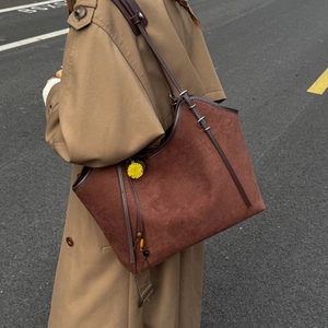Close-up of brown suede tote bag with yellow floral charm and leather shoulder strap