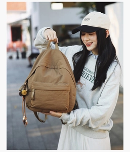 Detailed close-up of brown nylon backpack featuring ethnic style pompom charms and textures