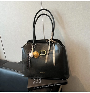 Detail of black suede tote bag featuring a gold buckle strap and decorative scarf