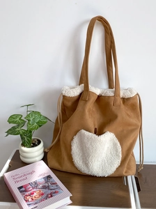 Detail of brown faux suede tote bag featuring a white sherpa heart pocket and drawstring