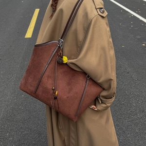 Brown suede tote bag with fringe charm worn by model in a stylish trench coat