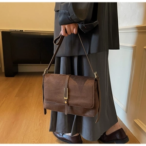 Detail shot of a brown suede rectangular handbag featuring a gold metal clasp and buckle