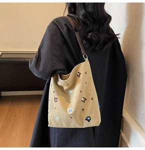 Detail of embroidered cat motifs on a khaki canvas tote bag with brown leather straps