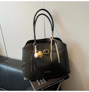 Detail of black suede tote bag featuring a gold buckle, brand logo and sports-themed charms