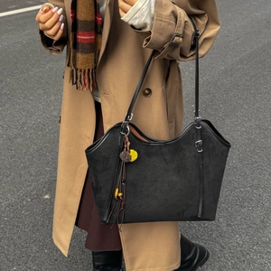 Detail of black suede tote bag featuring ethnic charms and a curved opening on a model