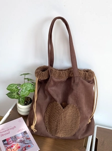 Brown suede tote bag with heart faux fur patch and drawstring detail on a wooden desk