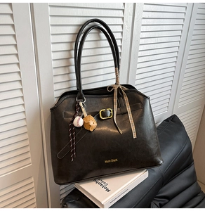 Close-up of large suede tote bag with leather strap detail and baseball charm accessory