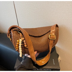 Detail of dark brown woven crescent bag featuring wooden bead tassel and gold buckle