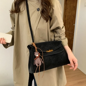 Detail of black suede shoulder bag with gold twist lock and cute brown bear charm
