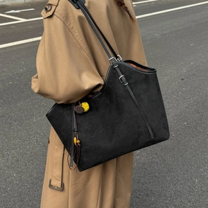 Detail of black matte tote bag with pompom charm on a khaki trench coat model