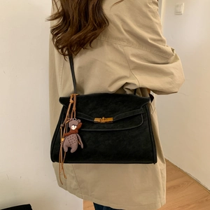 Detail of black suede shoulder bag with gold twist lock and cute bear charm pendant