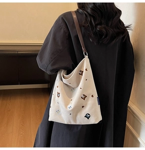 Detail of embroidered cats and bears on a beige canvas tote bag with brown leather handles
