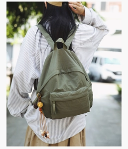 Olive green nylon backpack detail showing ethnic charm tassel and durable canvas texture