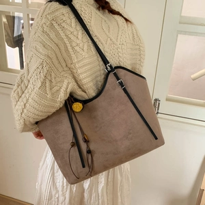 Close-up of taupe suede tote bag with floral pendant and wood bead detail on sweater