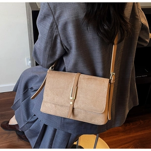 Close-up of camel suede messenger bag with gold hardware on a gray blazer background