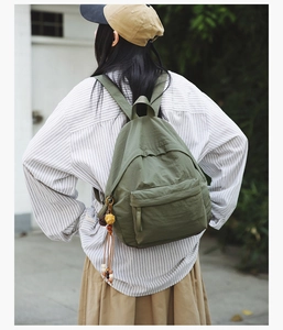 Detail of army green nylon backpack with ethnic style tassel and wooden bead charm