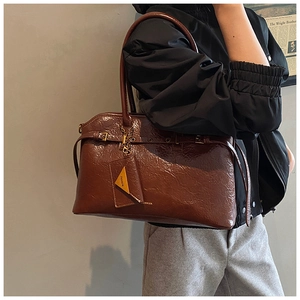 Detail of a brown glossy leather tote bag with vintage strap and gold chain accessories