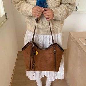Detail view of brown vintage suede tote bag with decorative pompom and adjustable strap