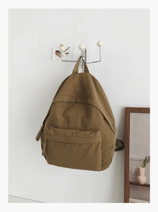Minimalist mustard yellow backpack hanging on a wall hook in a home setting scene