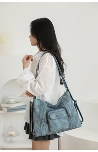 Detail of vintage denim tote bag with silver rivets and utility front pocket on a model