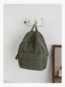 Detail view of olive green nylon backpack showing front zip pocket and textile texture