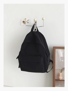 Minimalist black large-capacity canvas backpack hanging on a white wall hook