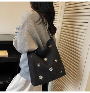 Detail of embroidered cat patterns on a large black canvas tote bag worn by a model