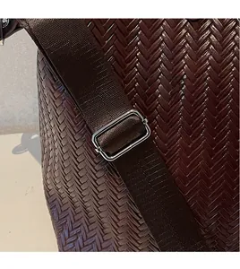 Détail d'un sac de voyage tressé marron foncé montrant la bandoulière réglable en toile