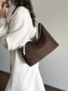Schicke hobo-tasche aus dunkelbraunem wildlederimitat mit perlenanhänger an einem beige-mantel