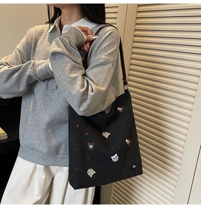 Detail view of black canvas tote bag with cute cat embroidery and brown leather straps